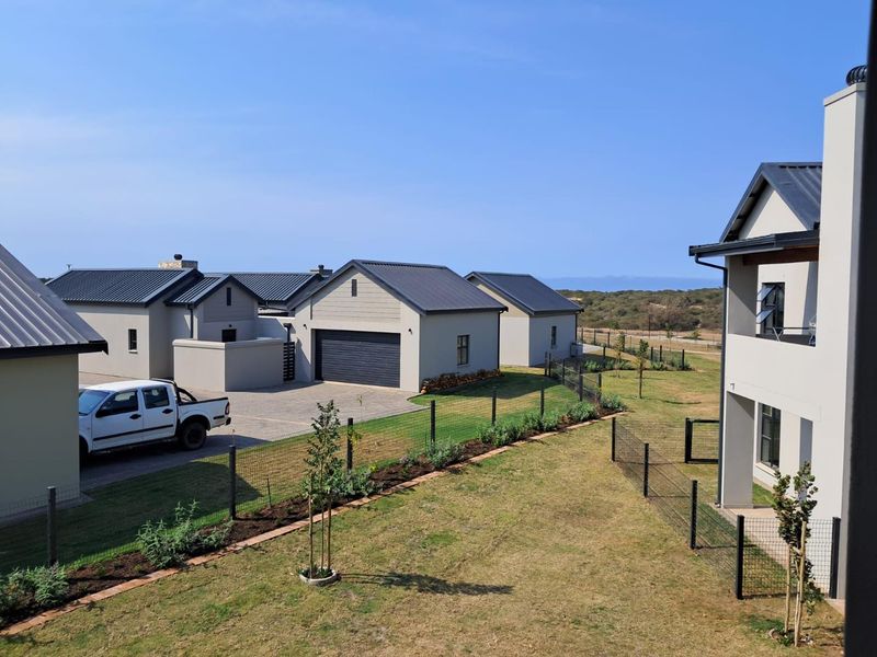 An elevated view of a modern residential complex featuring metal-roofed buildings, paved driveways, and landscaped garden areas with wire fencing.