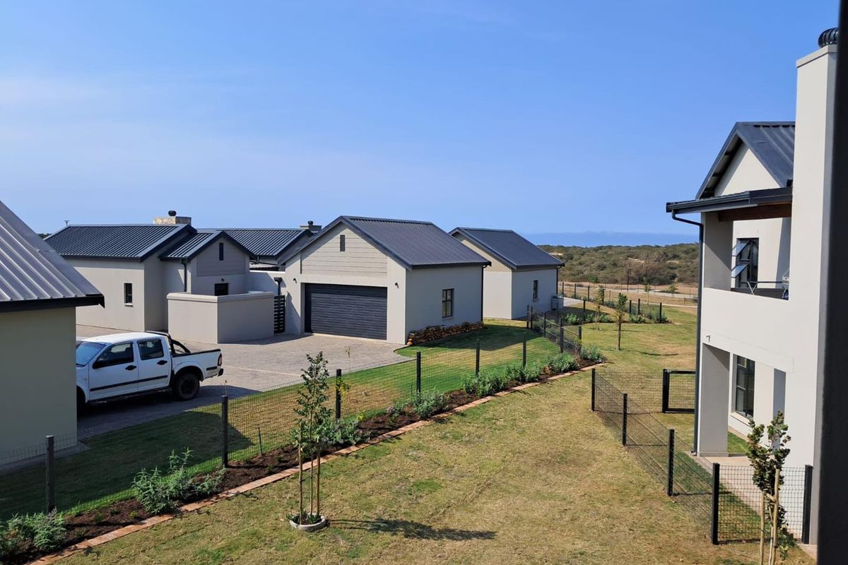 An elevated view of a modern residential complex featuring metal-roofed buildings, paved driveways, and landscaped garden areas with wire fencing.