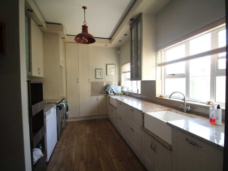 A well-appointed scullery featuring farmhouse sink, stone countertops, ample built-in cabinetry, and timber-look flooring, providing a functional and stylish secondary kitchen workspace.