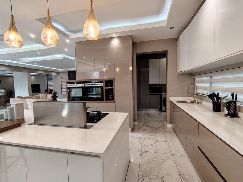 Modern open-plan kitchen featuring high-gloss cabinetry, stone countertops, a central island with integrated hob and extractor, and an adjacent scullery area.