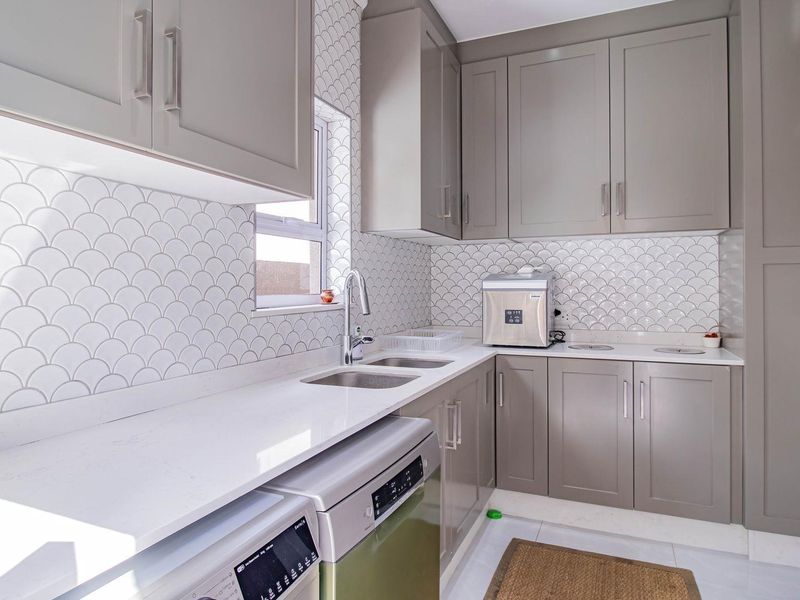 Modern scullery featuring sleek grey cabinetry, white quartz countertops, and a stylish scalloped tile backsplash with a double basin sink.