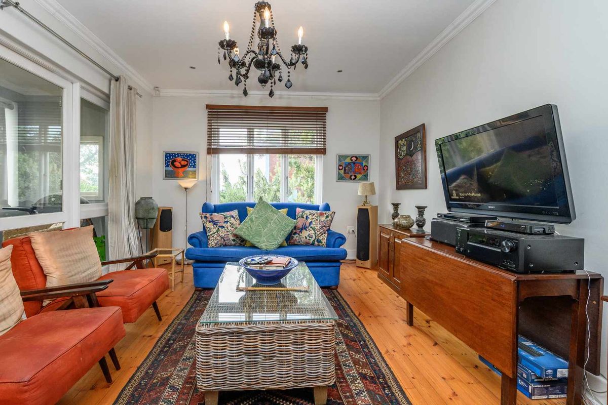 A cozy living room featuring polished timber flooring, large windows with wooden blinds, and a classic chandelier, offering a warm and inviting atmosphere.