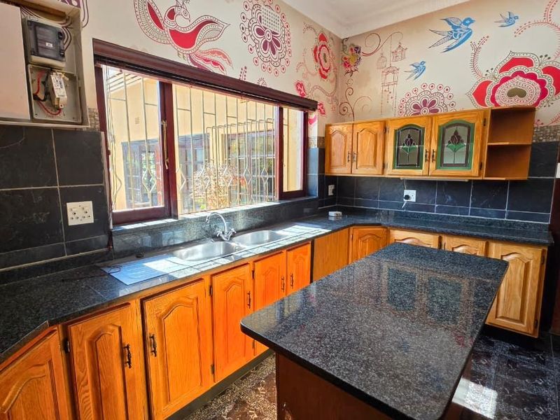 A functional kitchen featuring wooden cabinetry, granite countertops, a central island, and a double basin sink, with security bars on the window.