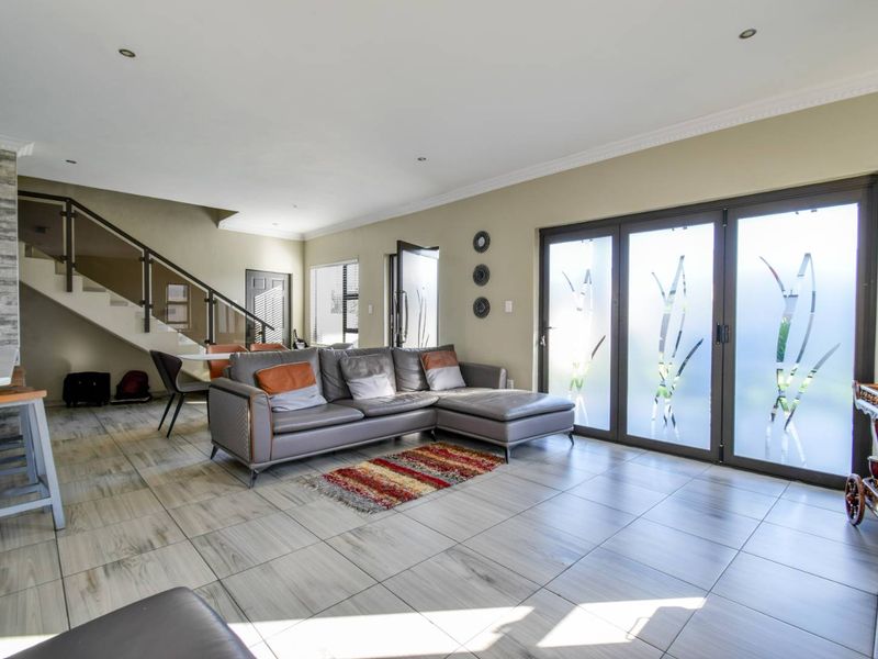 Spacious open-plan living area featuring modern tiled flooring, a striking staircase with glass balustrade, and large sliding doors leading to the exterior.