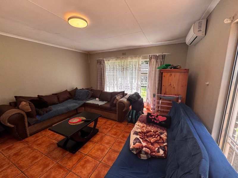 A living room featuring tiled flooring, an installed air conditioning unit, and ceiling lighting, offering a functional space with potential for cosmetic updates.
