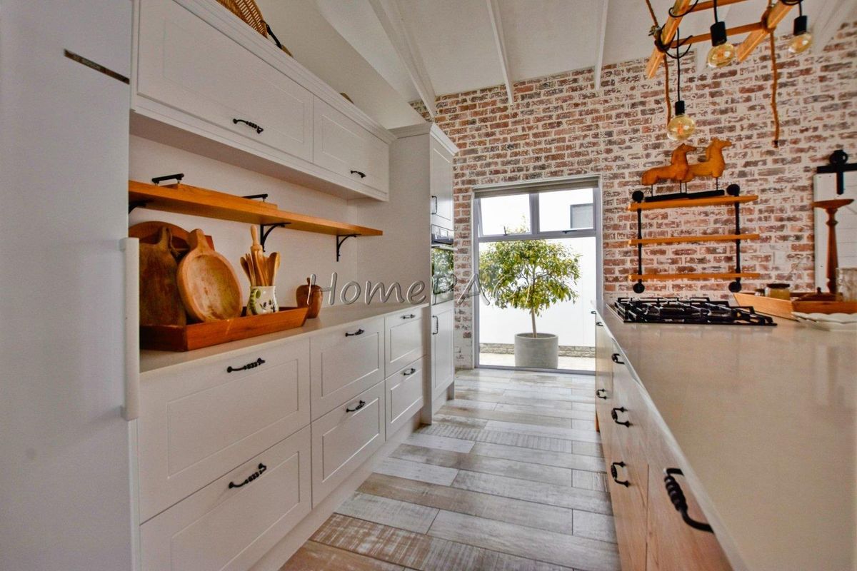A modern kitchen featuring white cabinetry, stone countertops, a gas hob, and a rustic exposed brick feature wall with tiled flooring.