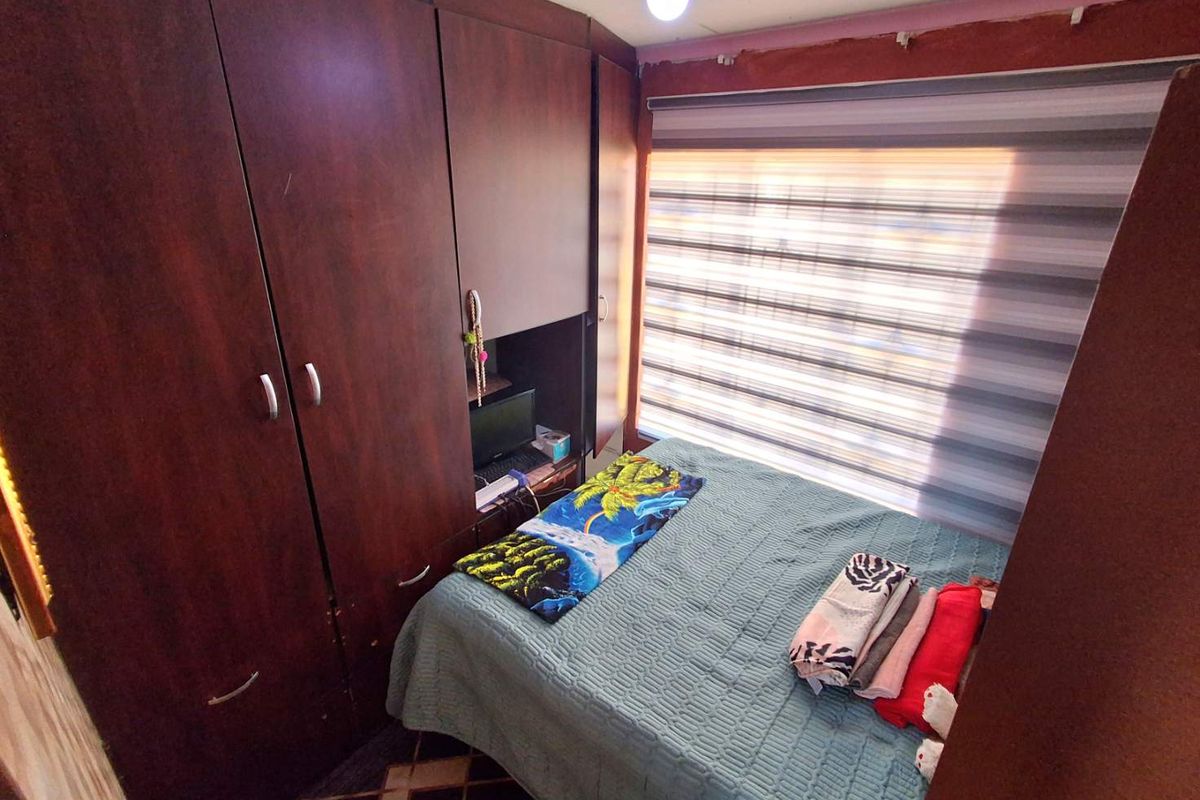 A compact bedroom featuring a large built-in wardrobe and modern roller blinds, requiring minor cosmetic repairs to the ceiling and wall finishes.