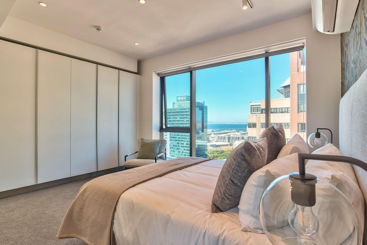 Modern bedroom featuring extensive built-in cupboards, plush carpeting, and large windows offering expansive city and ocean views.