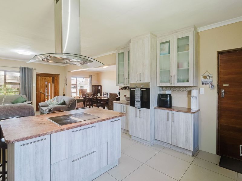 Open-plan kitchen featuring a central island with a hob, stainless steel extractor fan, built-in oven, and light wood-grain cabinetry with tiled flooring.