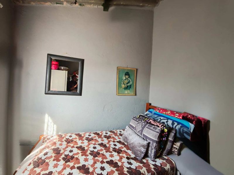 A bedroom featuring plain walls and a visible ceiling section showing signs of wear and plaster damage.