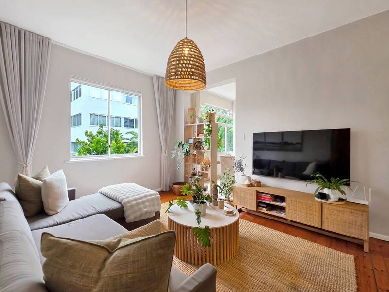 A bright and well-maintained living room featuring hardwood flooring, neutral walls, and large windows that provide ample natural light.
