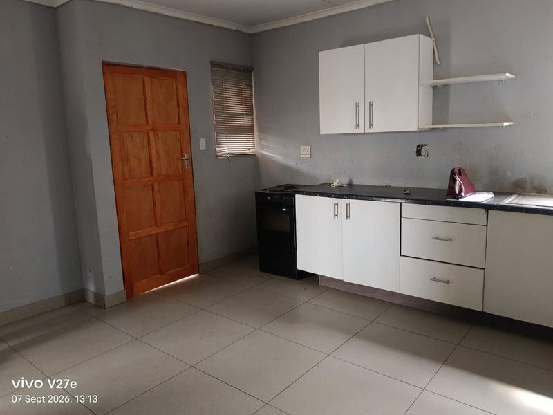 A compact kitchen featuring white cabinetry, dark laminate countertops, a freestanding stove, and tiled flooring, requiring minor cosmetic updates and finishing touches.