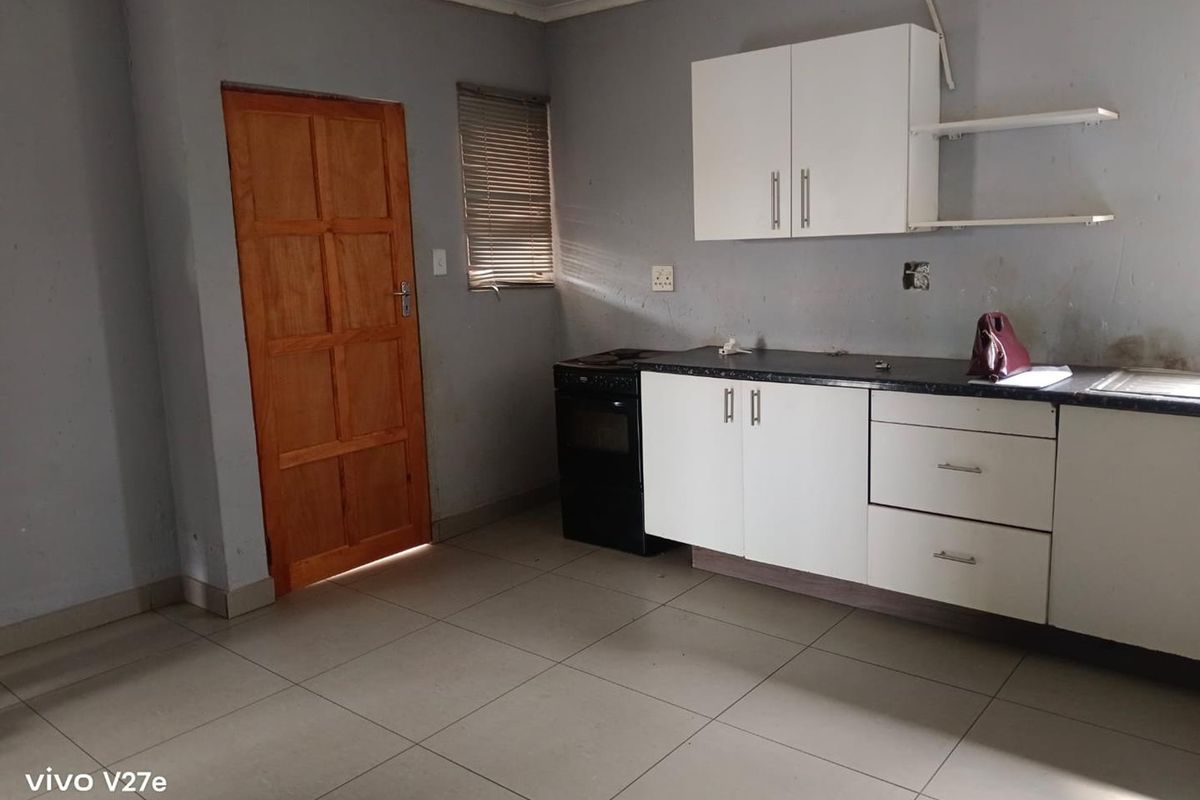 A compact kitchen featuring white cabinetry, dark laminate countertops, a freestanding stove, and tiled flooring, requiring minor cosmetic updates and finishing touches.