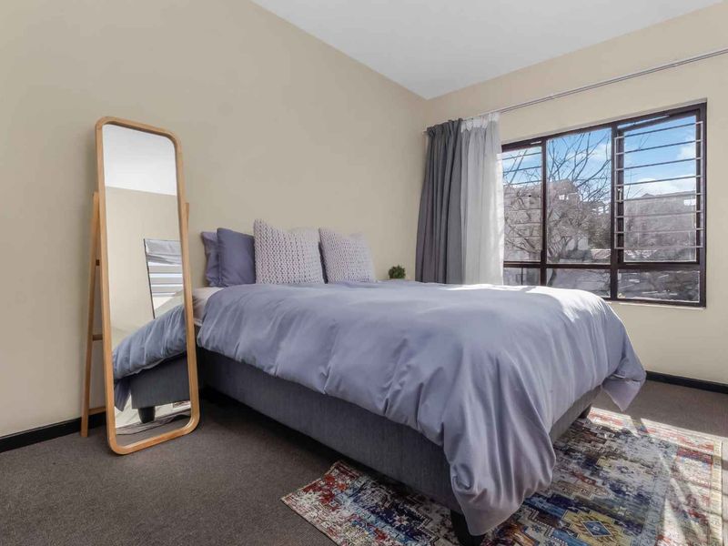 A well-lit bedroom featuring carpeted flooring and a large window equipped with security bars, providing natural light and ventilation.