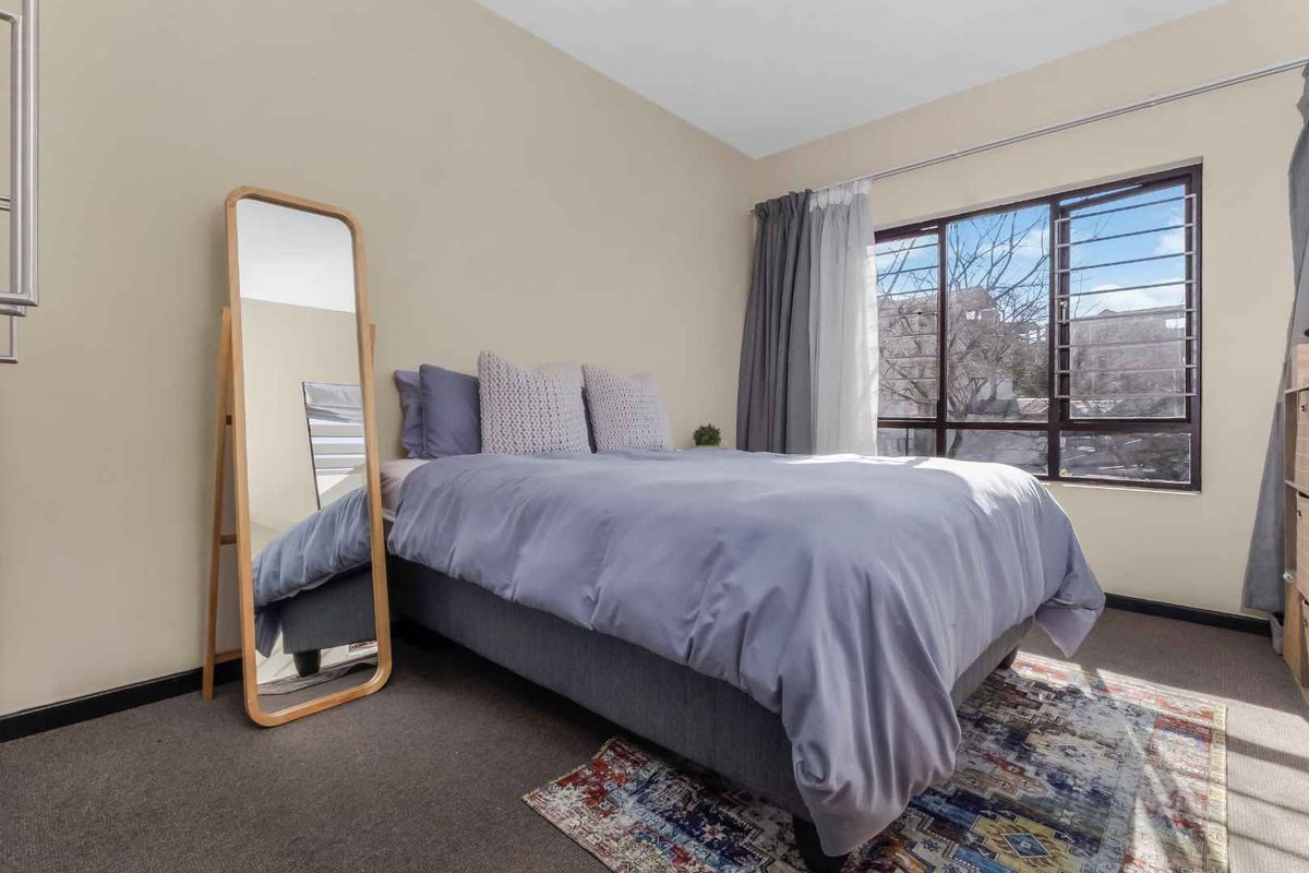 A well-lit bedroom featuring carpeted flooring and a large window equipped with security bars, providing natural light and ventilation.