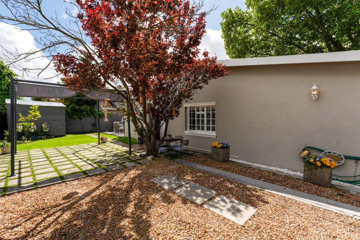 A well-maintained rear garden featuring a paved patio area, gravel landscaping, a pergola, and a storage shed.