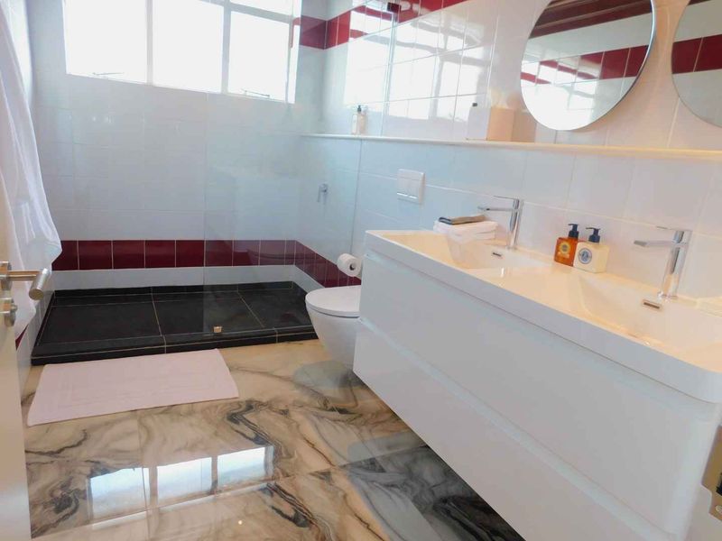 Modern bathroom featuring a double vanity, wall-mounted toilet, and a spacious walk-in shower with glass enclosure and contemporary tiled finishes.
