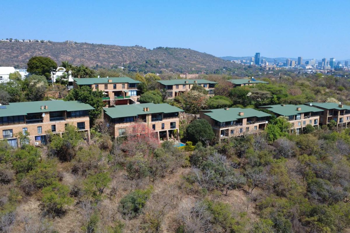 Aerial view of a residential complex featuring face brick buildings with green pitched roofs, nestled in a scenic, elevated hillside landscape.