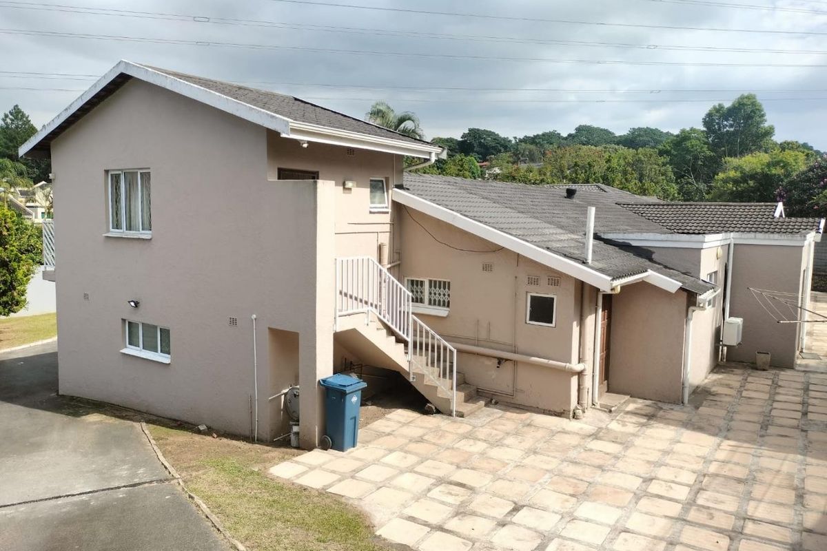 Rear exterior view of the house featuring a paved courtyard, external staircase, and tiled roof structure.