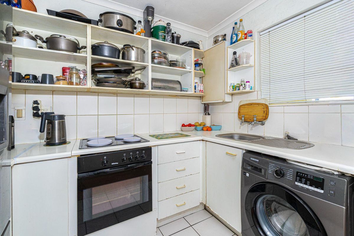 Compact kitchen featuring built-in oven, electric hob, stainless steel sink, and ample open shelving with tiled backsplash and laminate countertops.