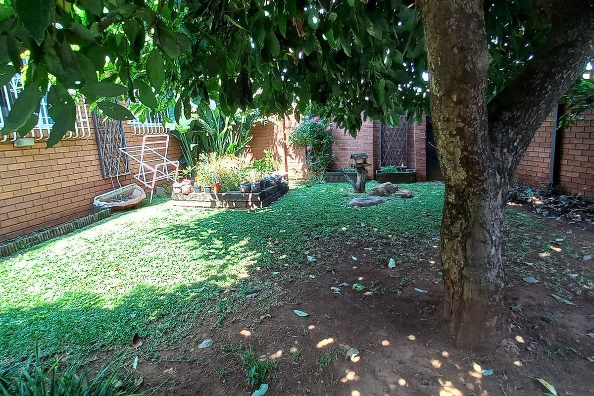 A private rear garden area featuring established trees, brick boundary walls, and a small raised planter bed.