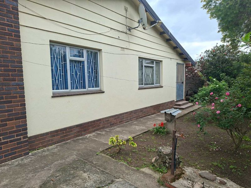 Rear exterior view of the house featuring a concrete pathway, brick plinth, and metal-framed windows with security bars.
