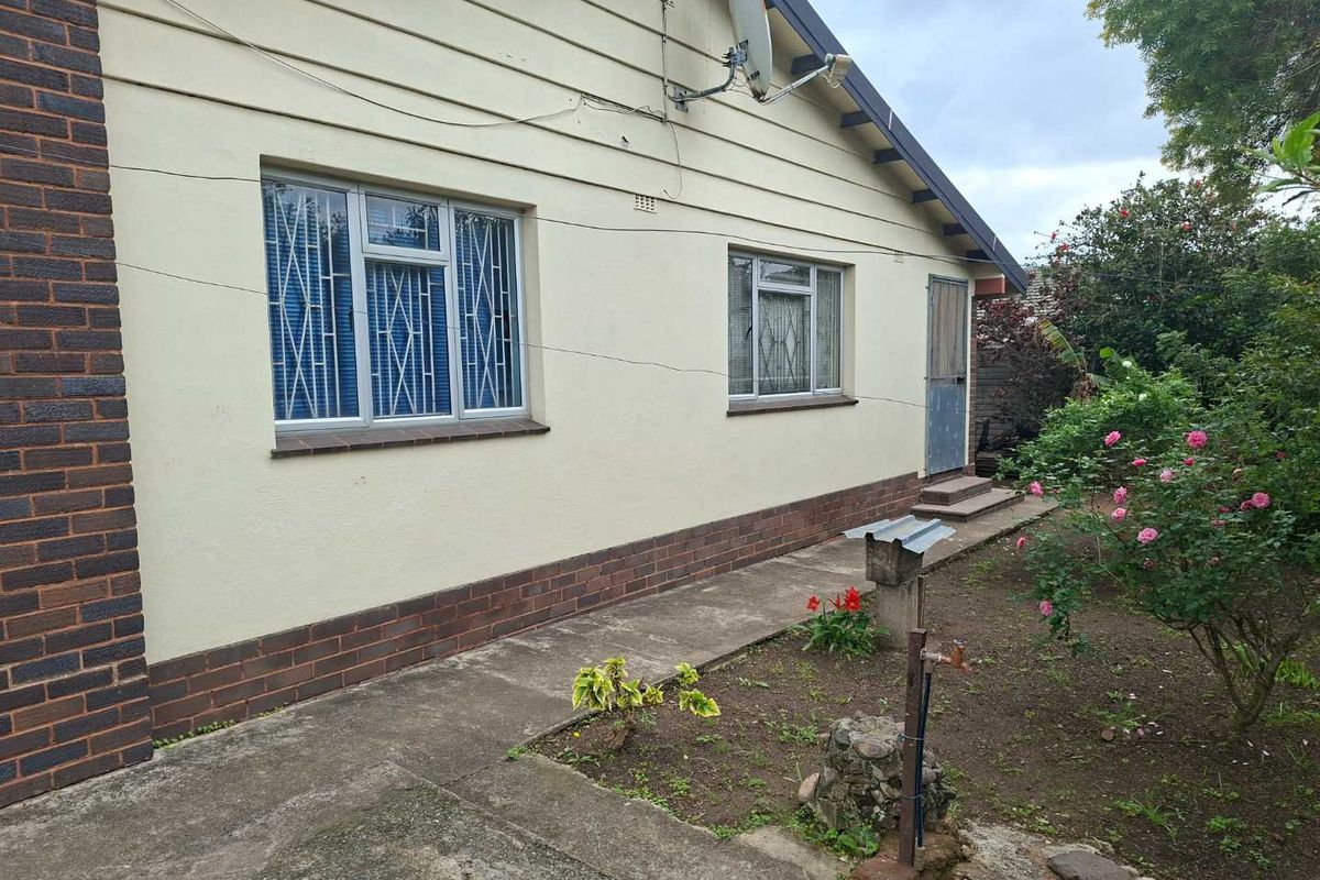 Rear exterior view of the house featuring a concrete pathway, brick plinth, and metal-framed windows with security bars.
