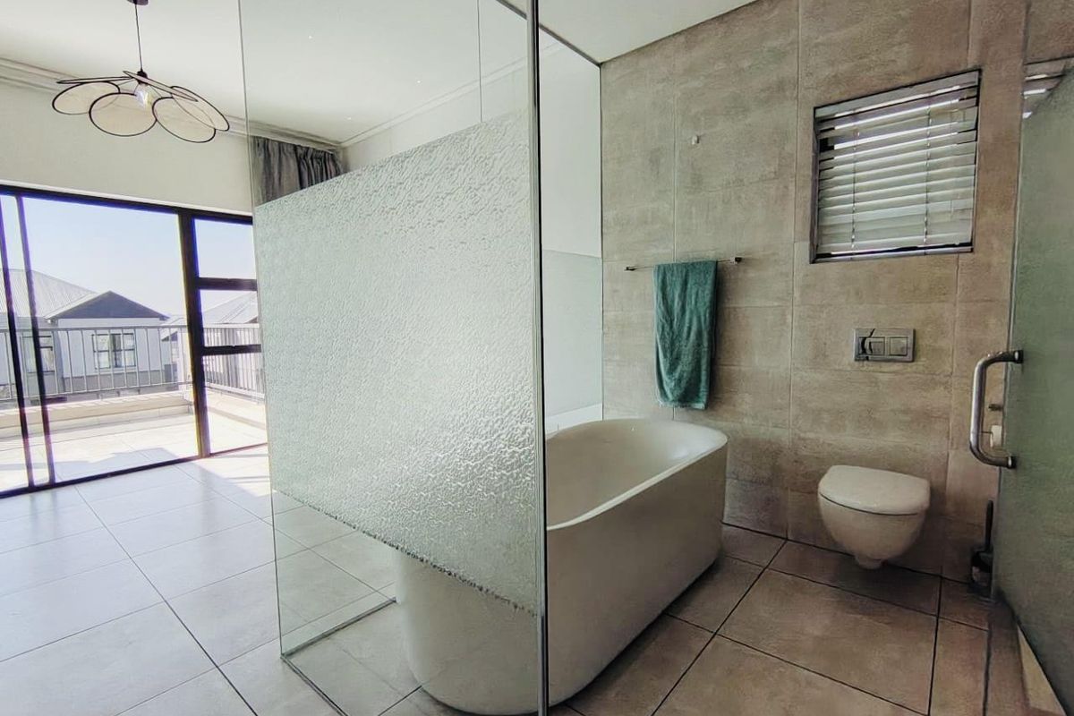 Modern bathroom featuring a freestanding bathtub, wall-mounted toilet, and large glass partition, with direct access to an outdoor balcony area.