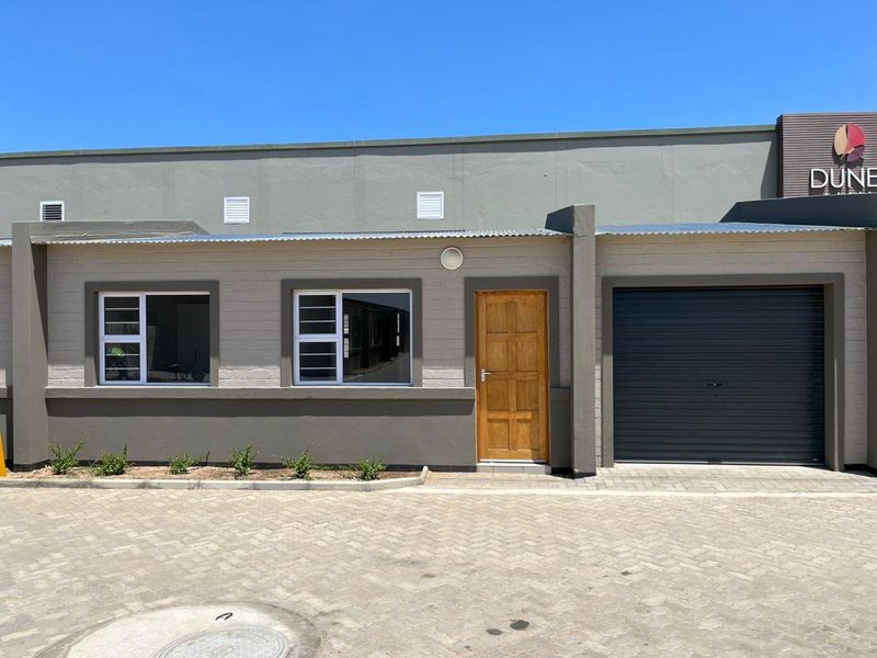 Front elevation of a modern townhouse featuring a paved driveway, roller garage door, timber entrance door, and aluminium-framed windows.