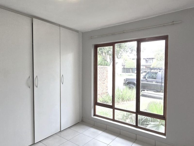 A bright, empty bedroom featuring neutral tiled flooring and ample built-in cupboard storage space.