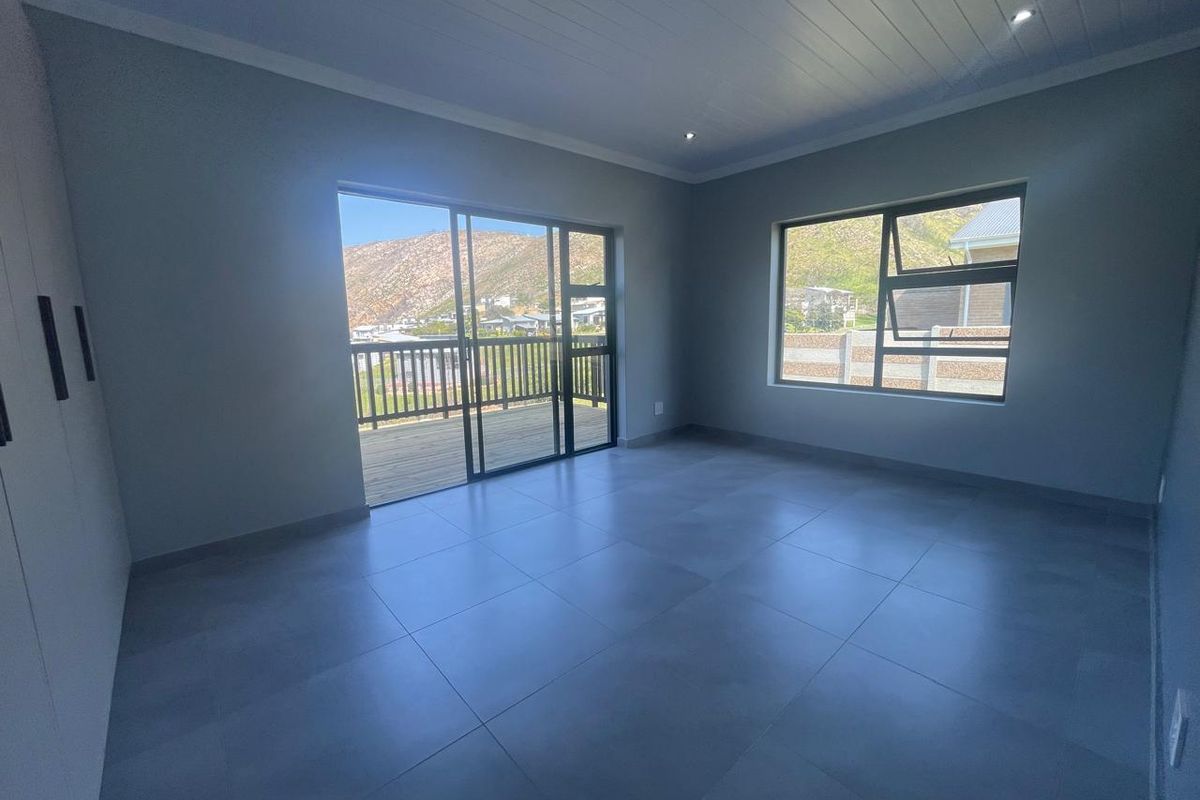 Spacious, modern bedroom featuring neutral tiled flooring, built-in cupboards, recessed lighting, and a sliding door leading to a private balcony with scenic views.