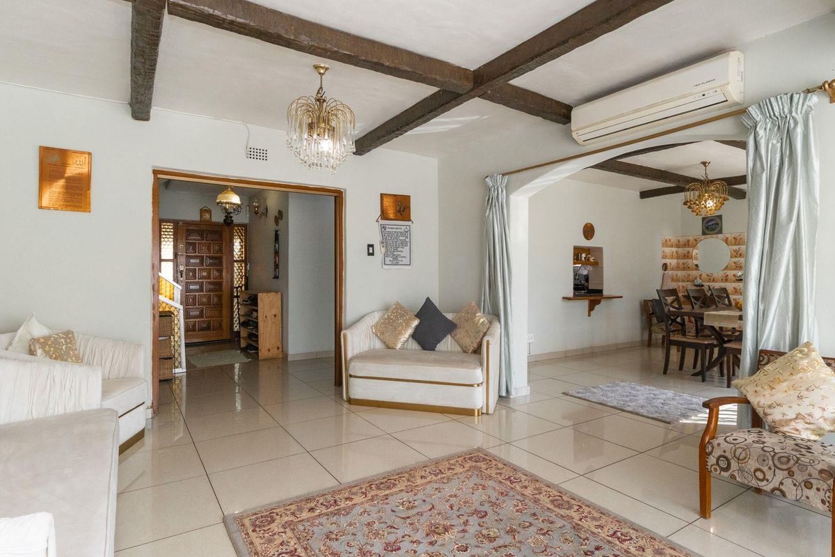 Spacious open-plan living and dining area featuring exposed timber ceiling beams, tiled flooring, and a wall-mounted air conditioning unit.