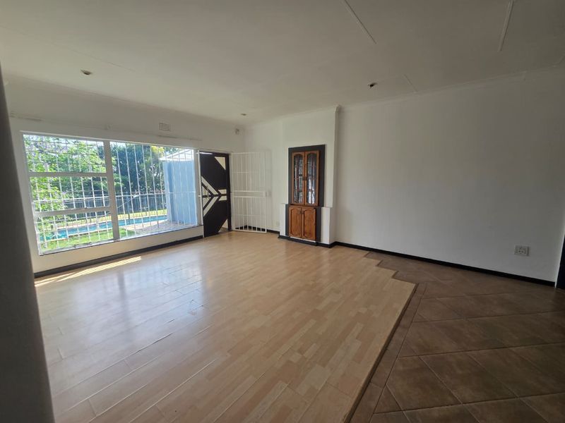 Spacious living area featuring a split-level floor design with laminate and tile flooring, built-in display cabinetry, and large windows with security bars.