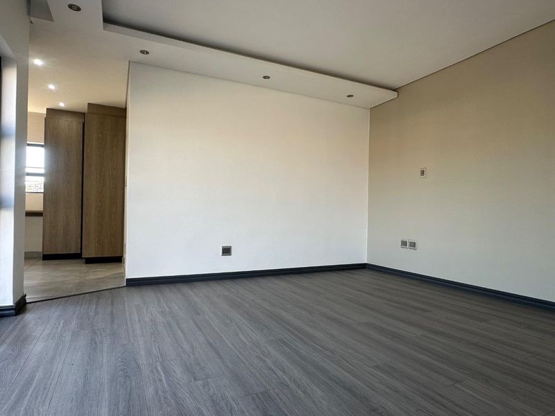 A bright, empty living area featuring modern laminate flooring, recessed ceiling lighting, and neutral wall finishes, providing a clean canvas for interior design.