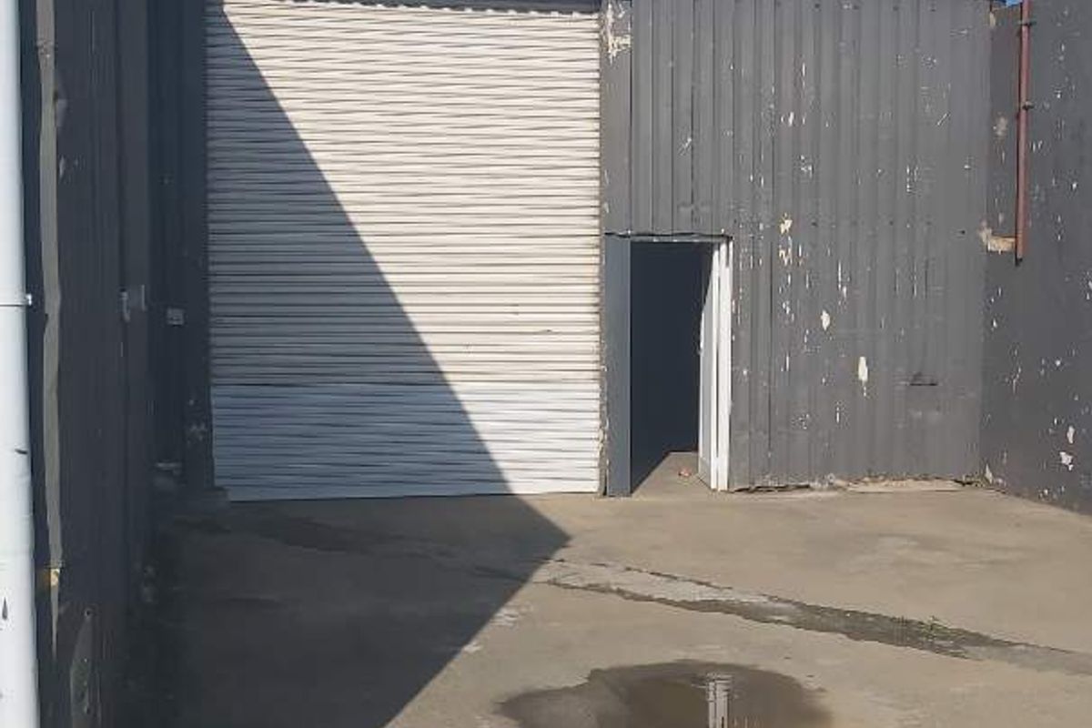 Industrial warehouse exterior featuring a roller shutter door, pedestrian access door, and corrugated metal cladding with a concrete apron.