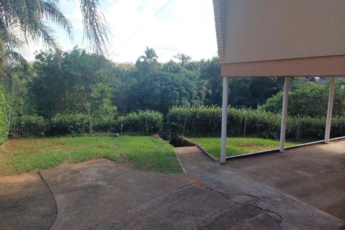 Rear exterior view featuring a concrete patio area, support columns, and a landscaped garden with wire mesh fencing.
