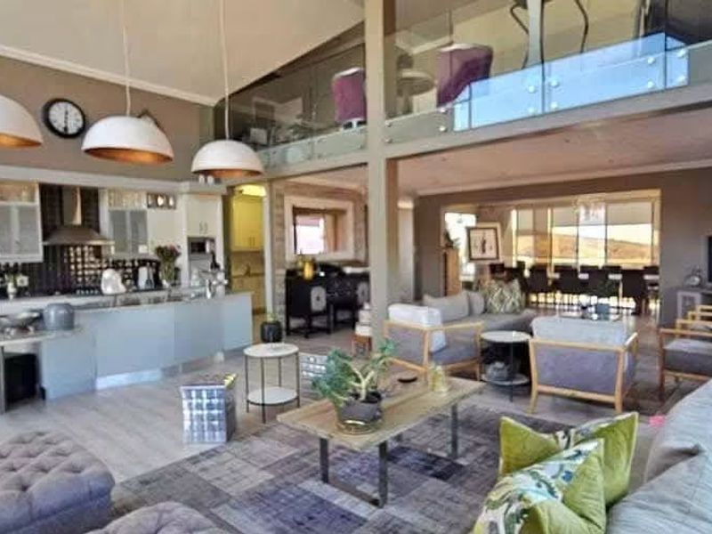 Spacious open-plan living area featuring a modern kitchen with island, integrated appliances, and a mezzanine level with glass balustrade overlooking the main living space.