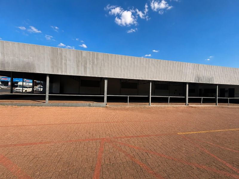Front elevation of a commercial building featuring a large metal-clad facade, covered walkway, and extensive paved parking area.