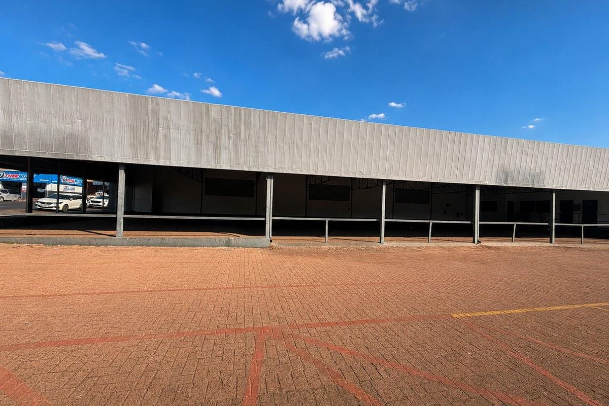 Front elevation of a commercial building featuring a large metal-clad facade, covered walkway, and extensive paved parking area.