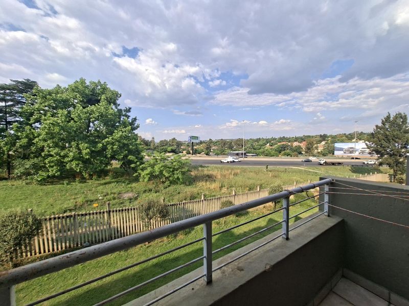 A balcony featuring a metal balustrade and tiled flooring, offering an elevated view of the surrounding landscape and nearby road.