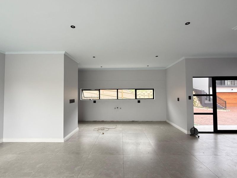 A spacious, modern open-plan living area featuring neutral walls, large format floor tiles, recessed lighting, and contemporary aluminium window and door frames.