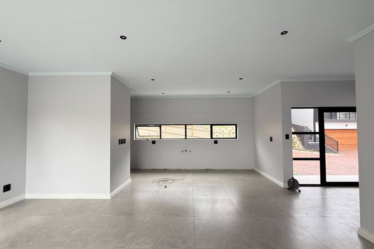 A spacious, modern open-plan living area featuring neutral walls, large format floor tiles, recessed lighting, and contemporary aluminium window and door frames.