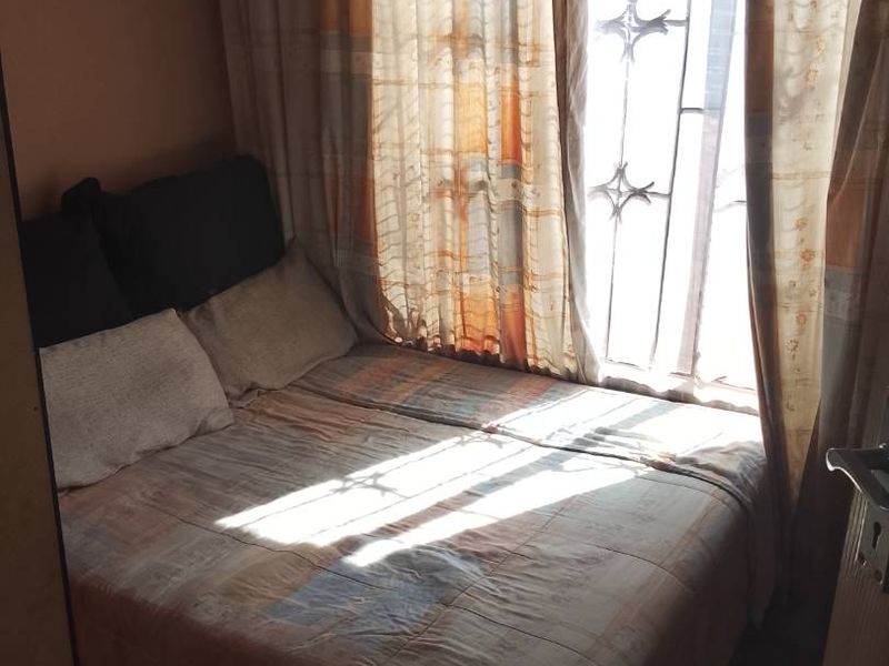 A compact bedroom featuring tiled flooring and a window fitted with a security gate, allowing natural light into the space.