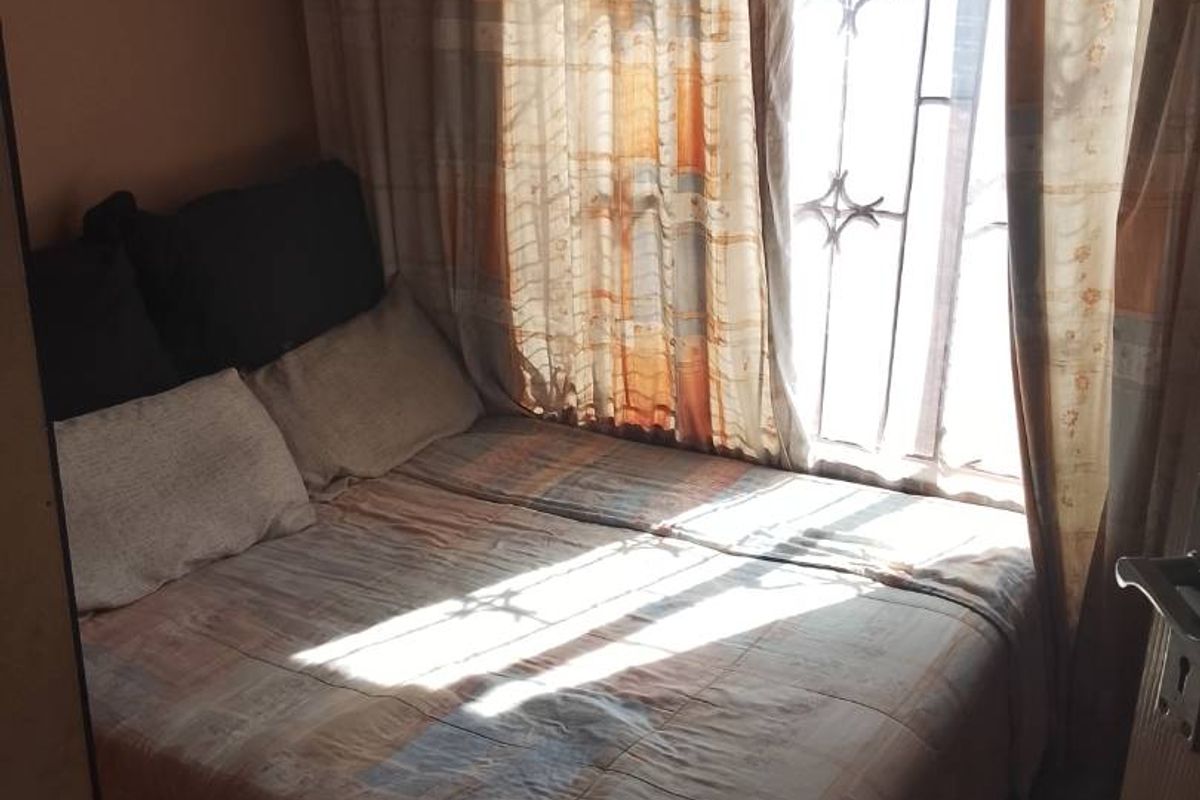 A compact bedroom featuring tiled flooring and a window fitted with a security gate, allowing natural light into the space.