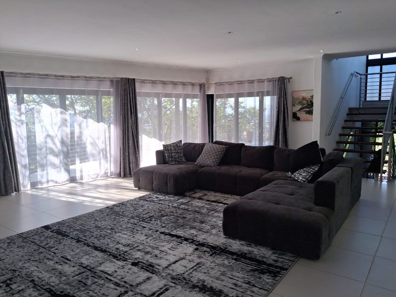 Spacious living room featuring large sliding glass doors, tiled flooring, recessed lighting, and an open staircase with a modern metal railing.