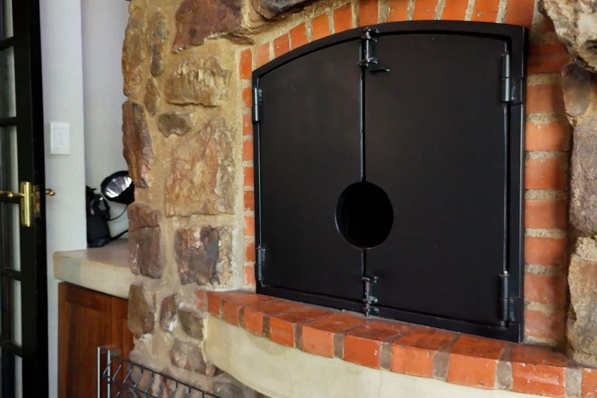 A rustic indoor fireplace featuring a stone and brick surround with a black metal door, adding character and warmth to the living space.