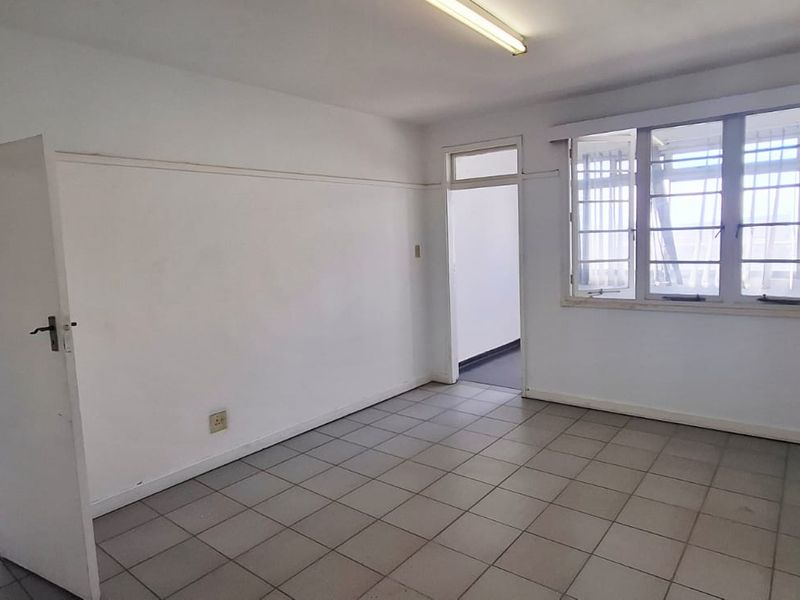 An empty, functional office space featuring tiled flooring, large multi-pane windows for natural light, and neutral wall finishes.