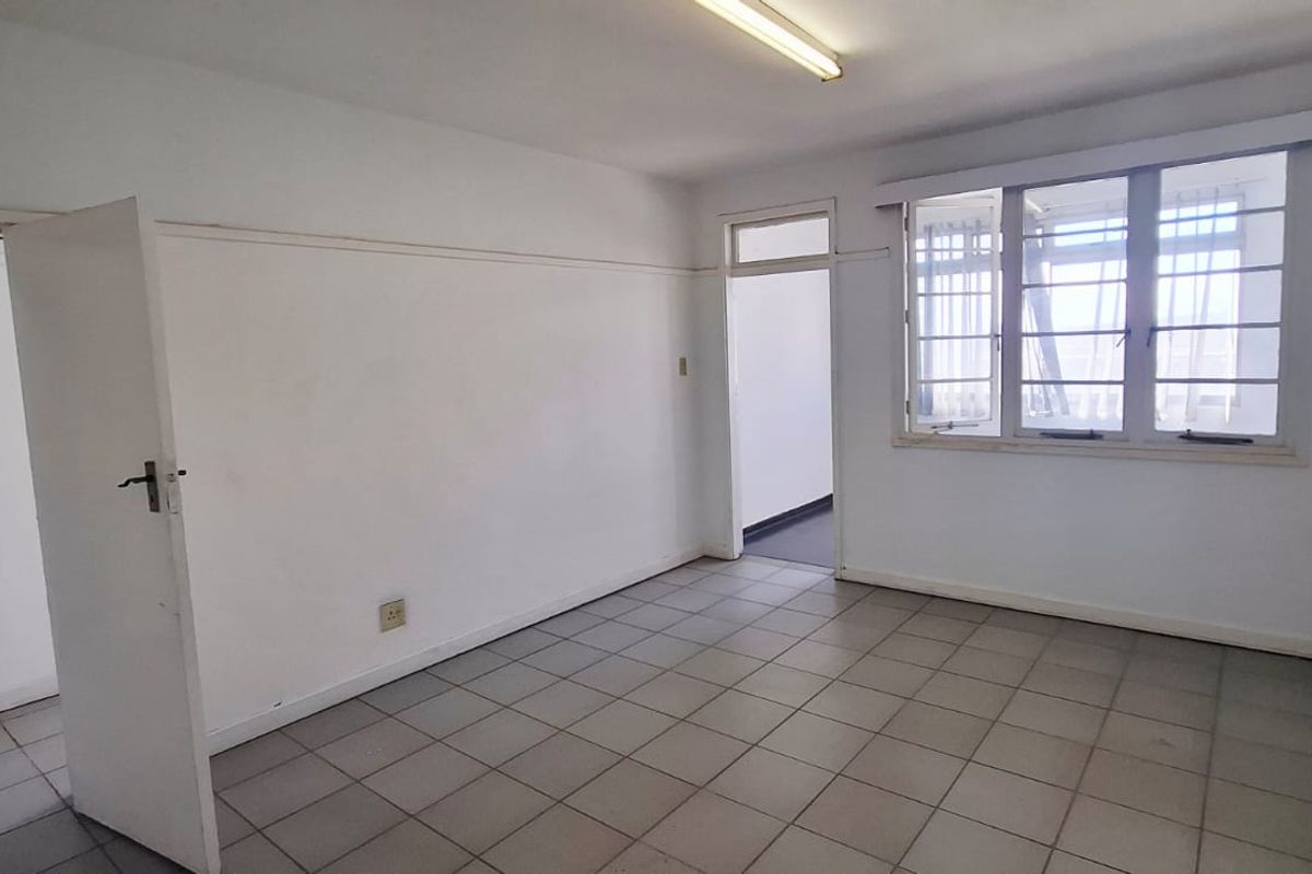 An empty, functional office space featuring tiled flooring, large multi-pane windows for natural light, and neutral wall finishes.