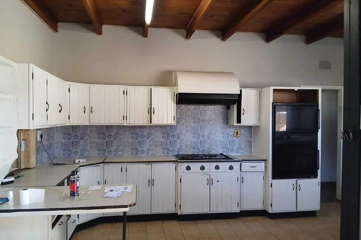 A dated kitchen featuring white cabinetry, patterned tile backsplash, built-in oven, and exposed timber ceiling beams, offering significant potential for modernization.