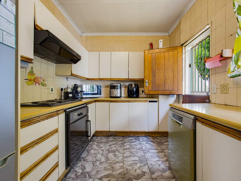 A functional kitchen featuring built-in cabinetry, laminate countertops, and tiled finishes, offering a practical layout with integrated cooking appliances and a window security gate.
